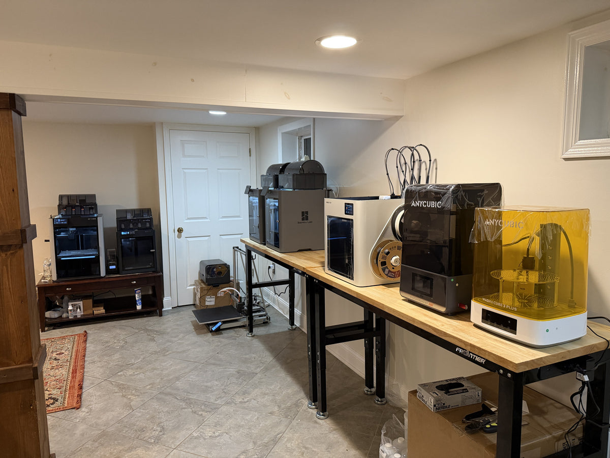 The Prinstey print farm in New Jersey — Bambu Lab FDM printers and an Anycubic resin printer with a wash and cure station on the workshop bench