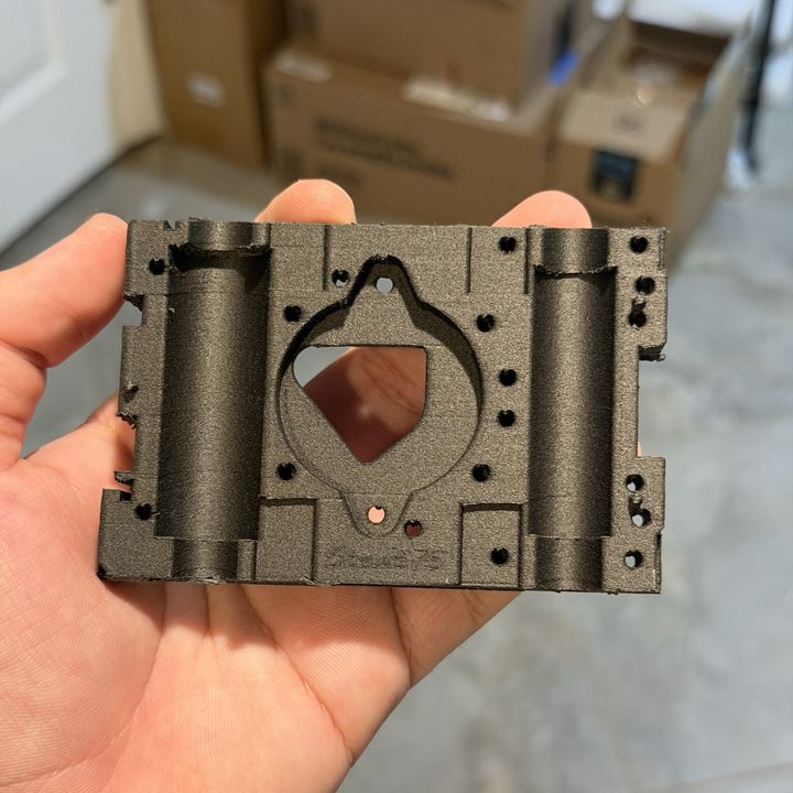 Black carbon-fibre nylon carrier plate for a 3D printer, held in a hand