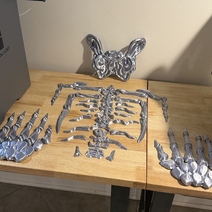 Silver silk PLA skeleton pieces for a costume laid out on a table: ribs, spine, pelvis and hands