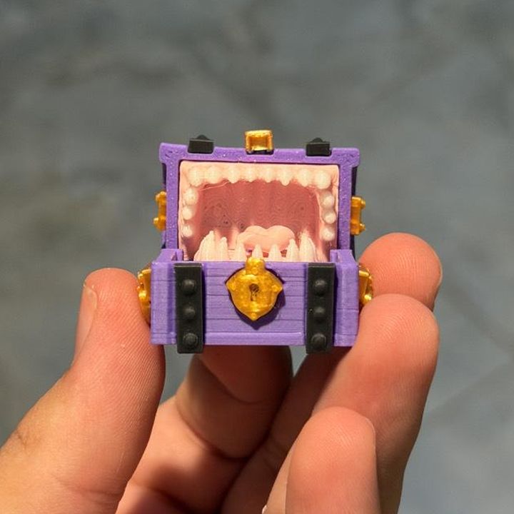 Purple mimic treasure-chest miniature with pink teeth and a gold clasp, held in a hand